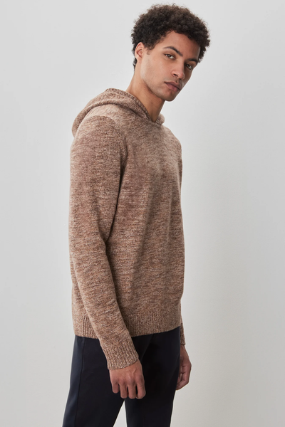 A man wearing the Robert Barakett Wildman Sweater and dark pants stands against a plain light gray background, looking slightly to the side.