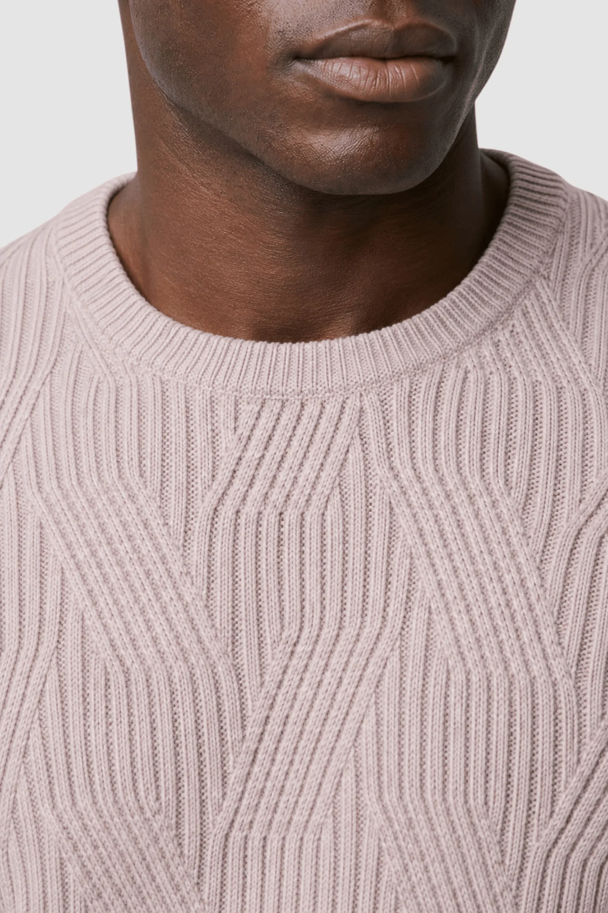 Close-up of a person wearing the Garnet Garrick Diamond-Pattern Crewneck Sweater 2622010 by Garnet, featuring a light beige hue and geometric ribbed knit design—perfect for men’s fall fashion. The photo highlights only the lower half of the face, neck, and upper chest, emphasizing the subtle elegance of this wool-blend sweater.