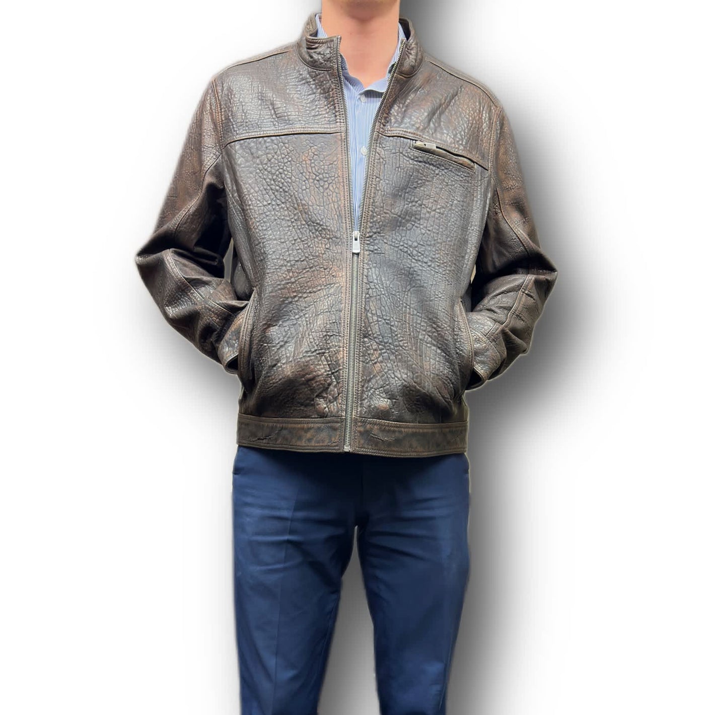 A man wearing a brown Missani leather jacket with a crew neckline and long sleeves, paired with blue trousers. The jacket features a zipper closure and multiple pockets.