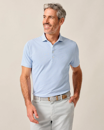 Man with gray hair wears the Johnnie-O Performance Polo-Stetsons, paired with a beige patterned belt and light gray pants, standing and smiling while looking to the side.
