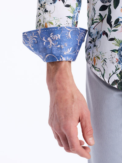 A person showcases the Robert Graham Briarcliff Woven Shirt Big & Tall, featuring a botanical print with blue cuffs, paired with light pants. Their right arm and hand are visible against a white background. The cotton-blend construction offers both comfort and style, embodying the signature look of Robert Graham.