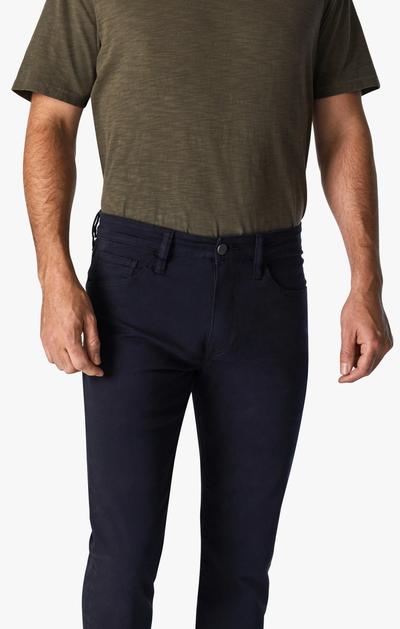 A man wearing an olive green short-sleeve t-shirt and the 34 Heritage Courage Twill Pant in a dark blue modern fit, standing with his arms relaxed by his sides against a plain background.