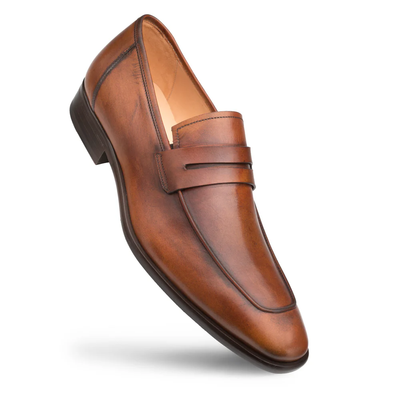 The Mezlan Calfskin Penny Loafer E20243 is a handcrafted men’s loafer made from brown calfskin leather, featuring a classic penny slot, low heel, and visible stitching. The shoe is positioned at an angle on a white background, exemplifying the refined style of Mezlan.