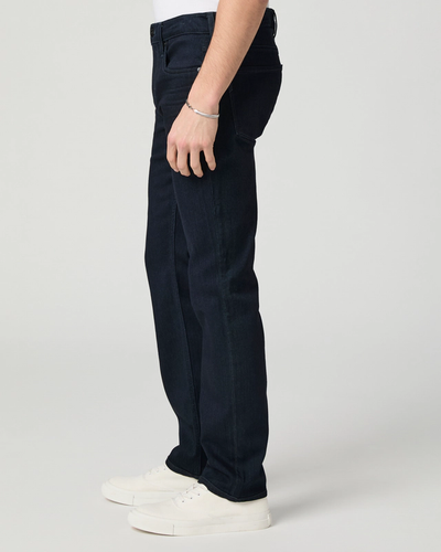Someone wearing Paige Federal Straight Slim Jeans from Paige, styled in a modern slim straight fit, with a silver bracelet and white sneakers, stands against a plain light background.