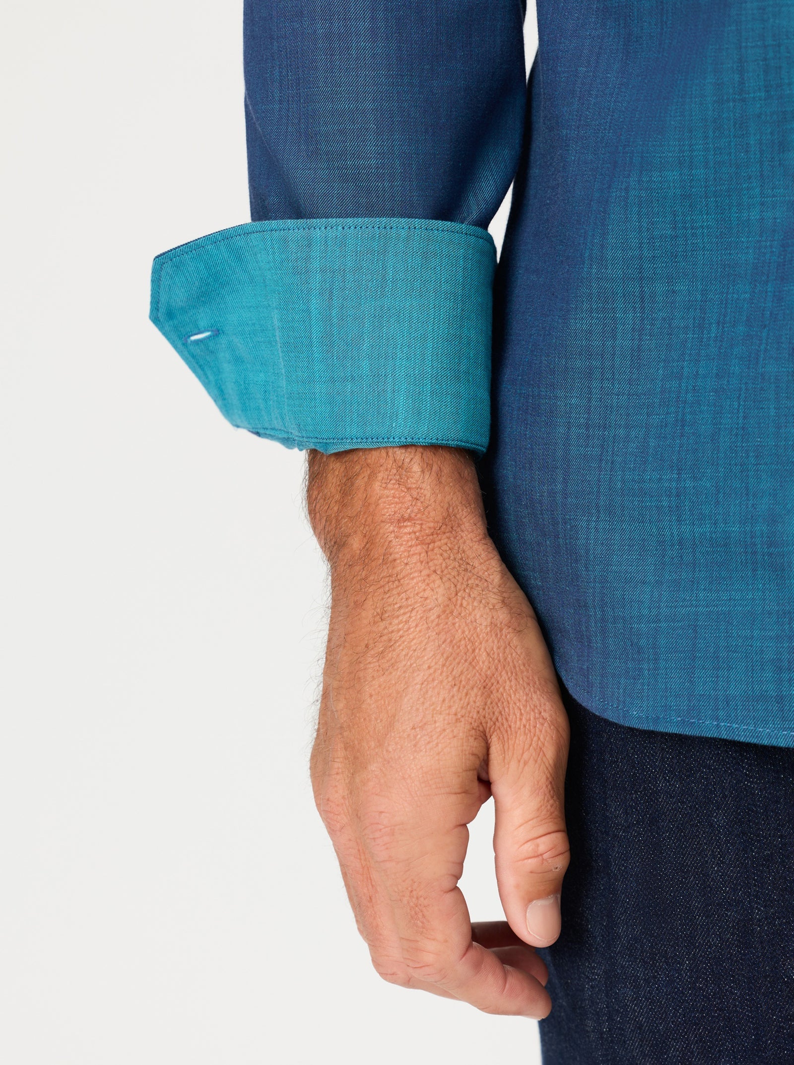 A person wearing the Robert Graham Kerrington Woven Shirt Big & Tall by Robert Graham, featuring a blue two-tone chambray design with turned-up cuffs that reveal a lighter blue inner lining and highlight its textured weave, paired with dark pants.