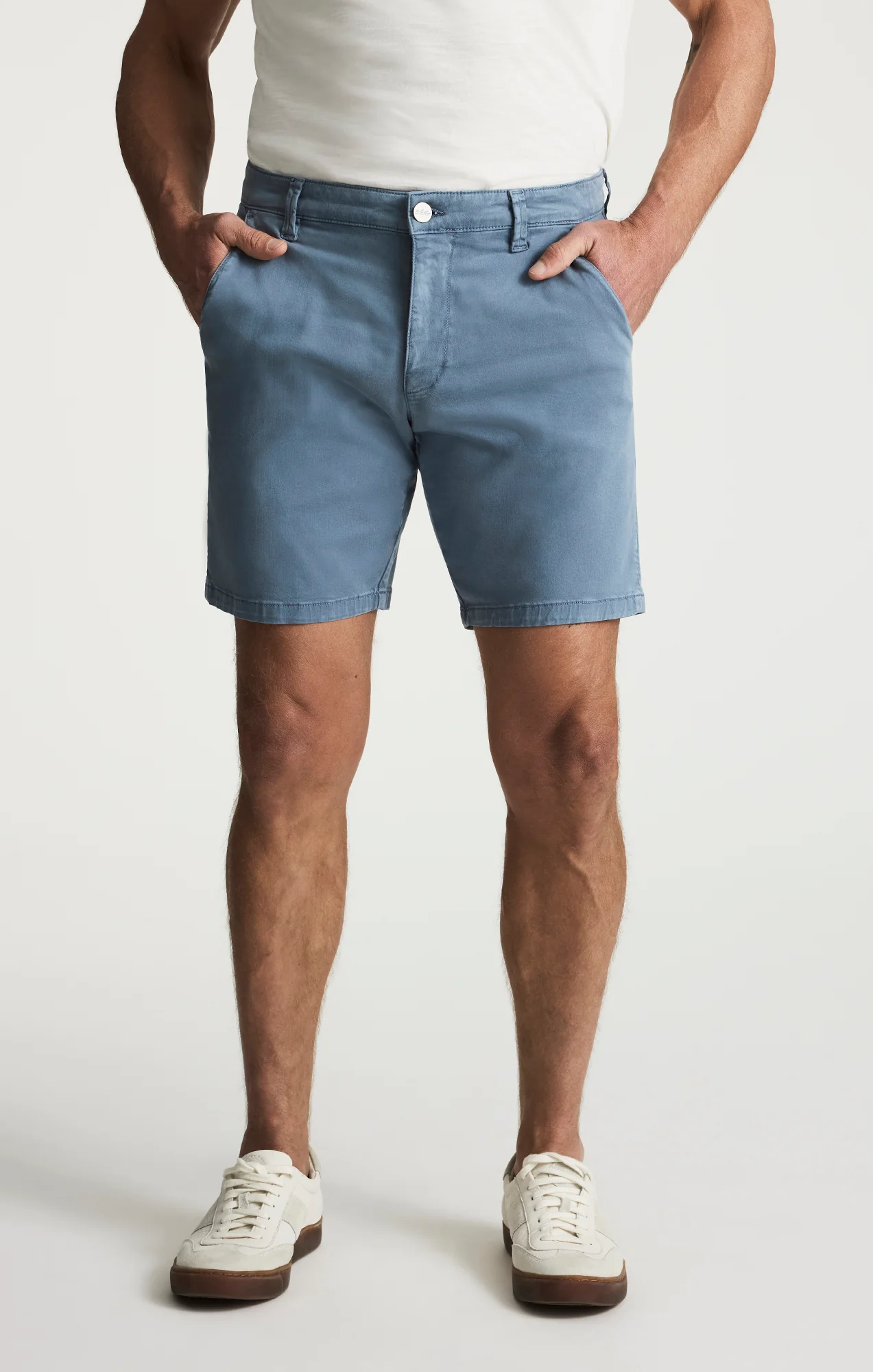 A man stands with hands in pockets, wearing a white t-shirt, white sneakers, and 34 Heritage Arizona Twill Shorts by 34 Heritage against a plain background.