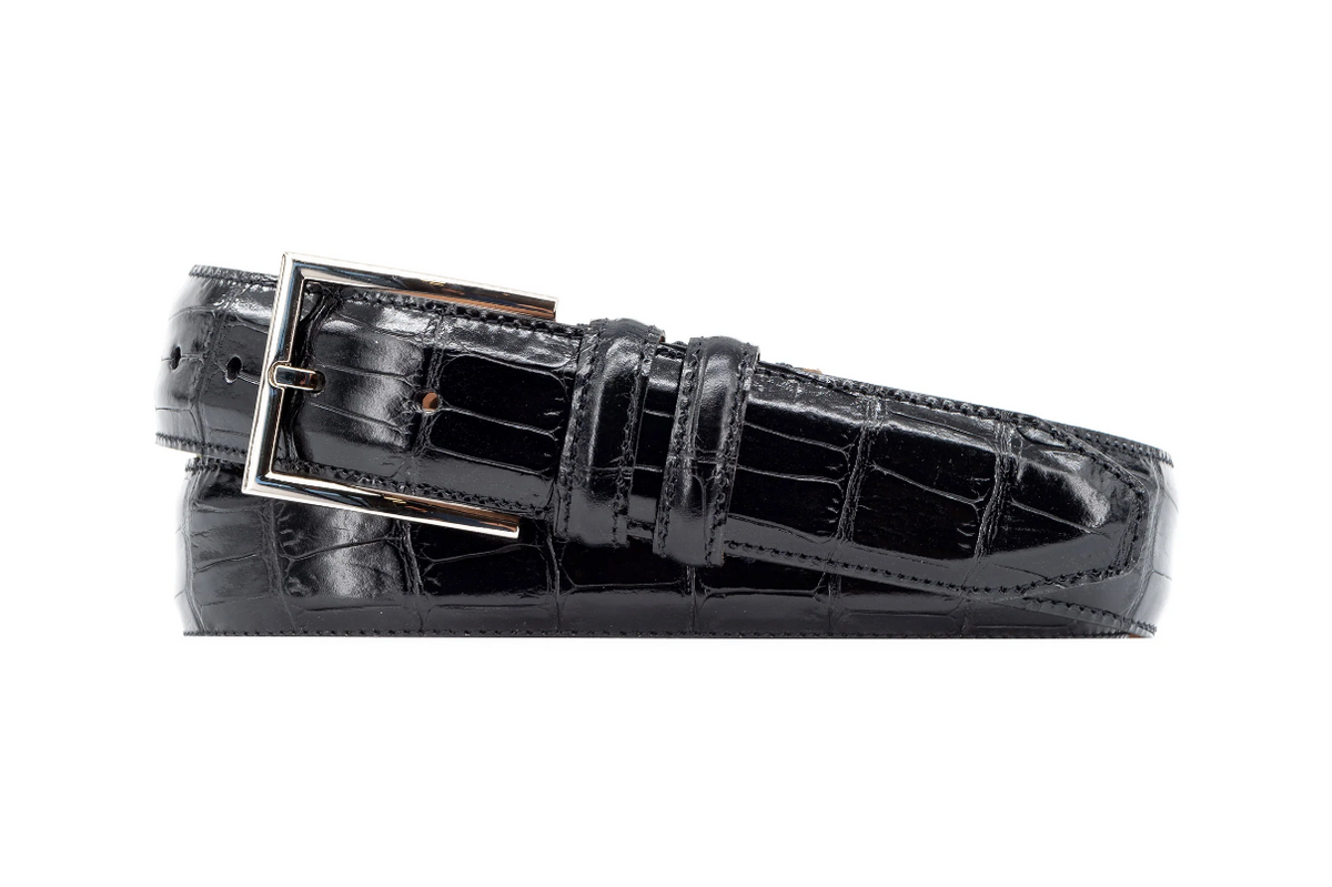 The Martin Dingman Alexander Alligator Leather Belt in black features a silver rectangular buckle and is neatly rolled against a white background.