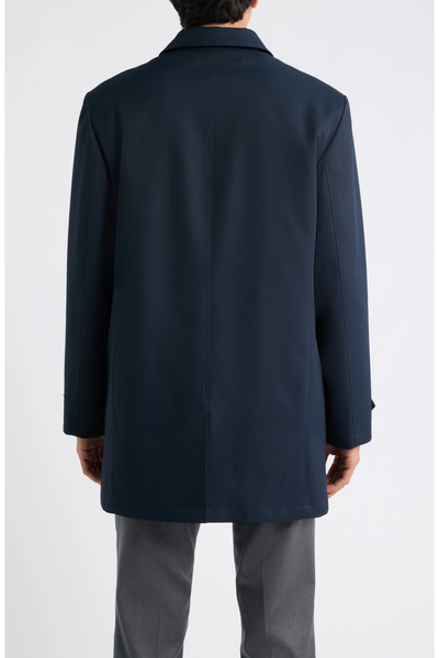 Back view of a person wearing a navy blue, mid-length Hart Schaffner Marx Milo Waterproof All-Weather Jacket and grey trousers.
