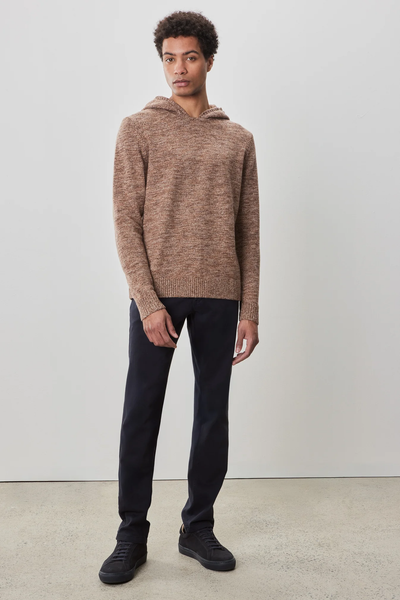 A man stands indoors against a plain wall, wearing the Robert Barakett Wildman Sweater, dark pants, and black sneakers.