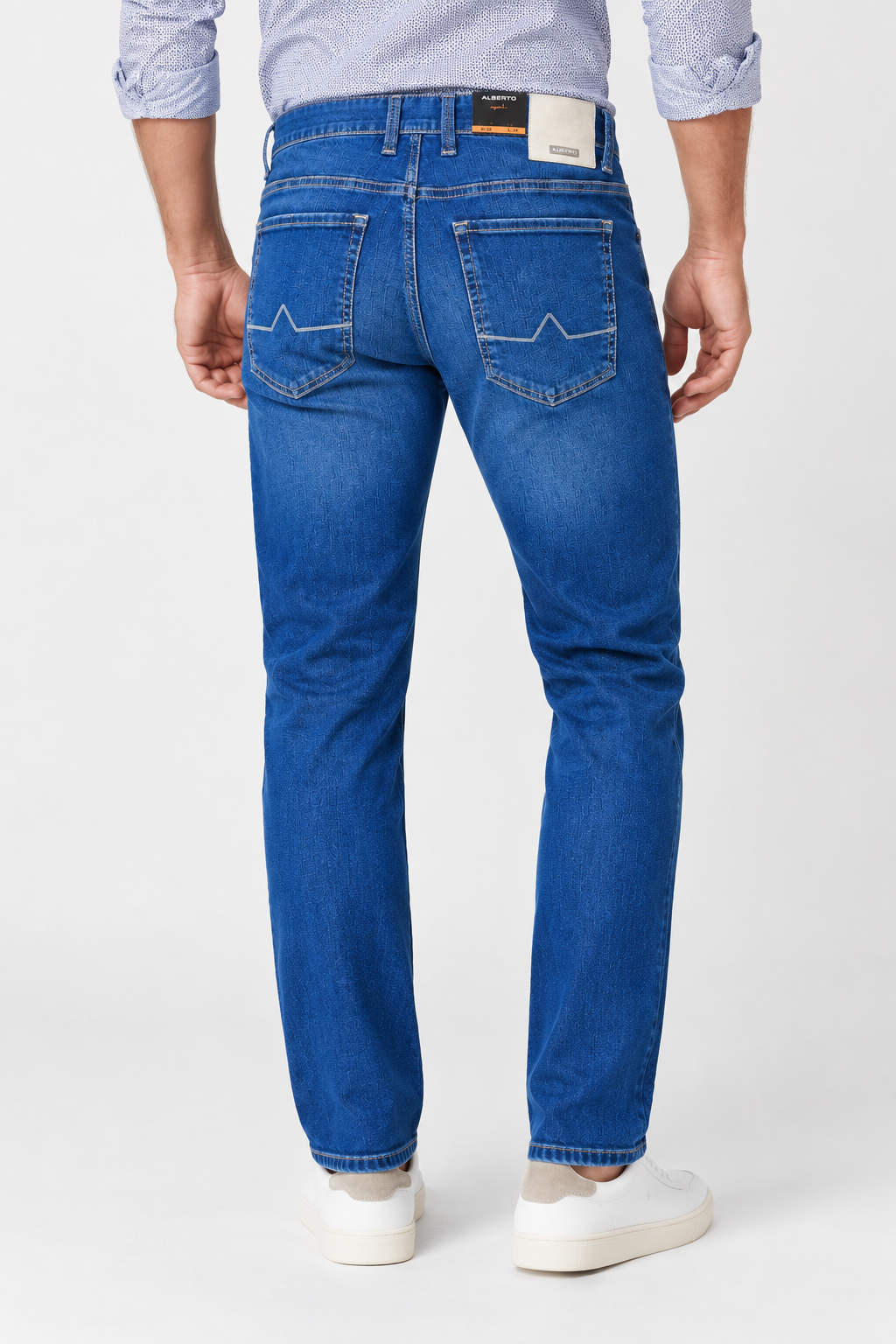 Back view of a person wearing Alberto Pipe 1984 Stretch Denim jeans with stitched pocket detailing, a light patterned shirt, and white sneakers.