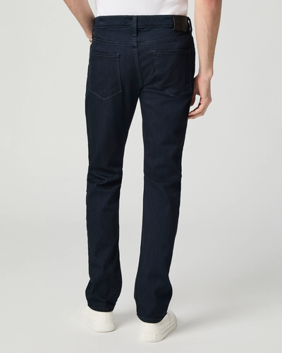 A person wearing Paige Federal Straight Slim Jeans by Paige in a dark wash and white shoes stands with their back to the camera against a plain background.