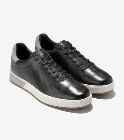 The Cole Haan GrandPro Angleace Sneakers by Cole Haan feature a black leather upper, white soles, grey heel accents, and perforated sides, shown against a plain white background.