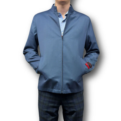 A person models the Mattarazi Coat Paolo, a blue zip-up jacket by Mattarazi, over a light blue shirt with hands in pockets and dark plaid pants, posed against a white background.