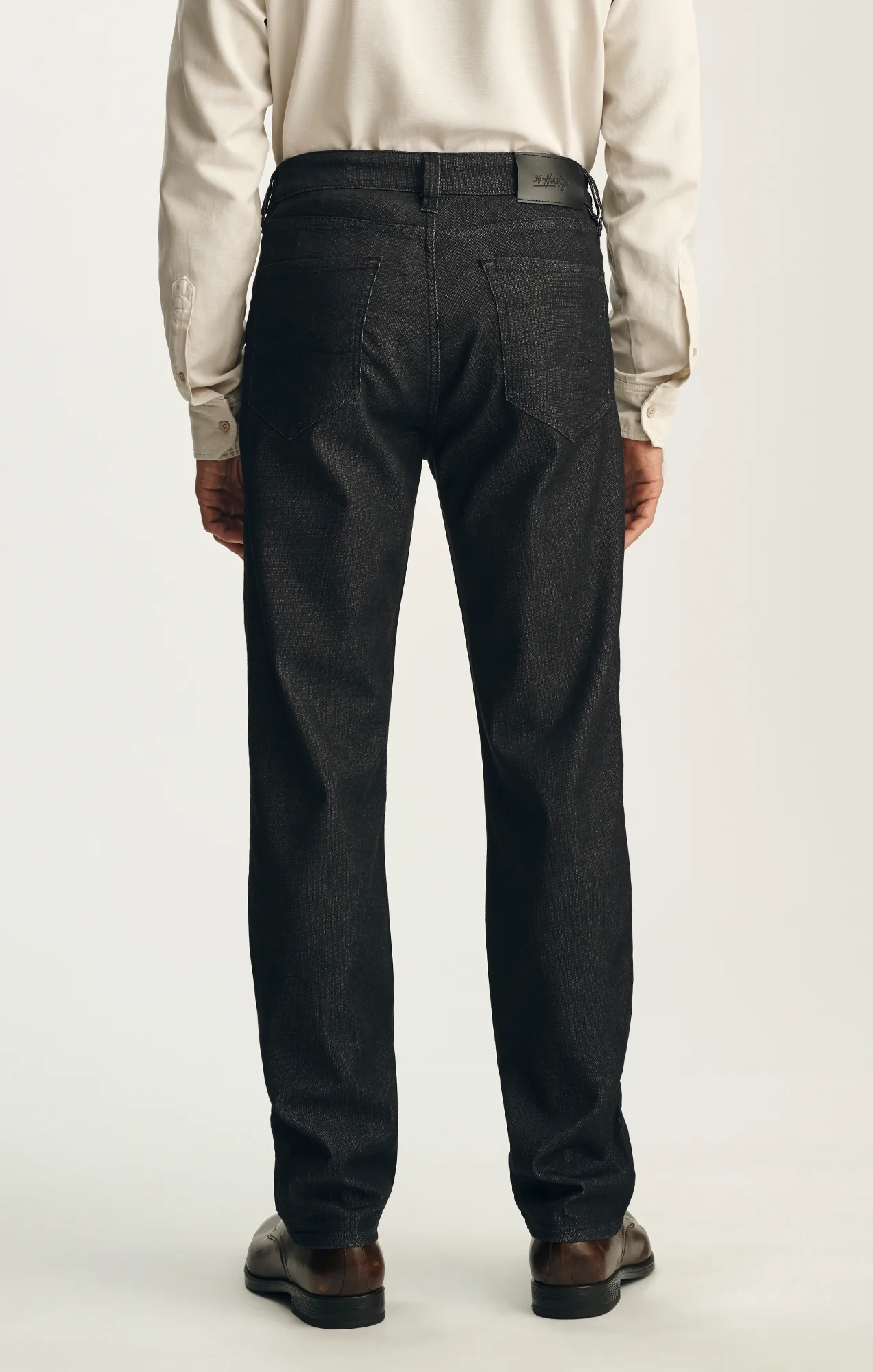 A person stands facing away, wearing a cream long-sleeve shirt, brown shoes, and 34 Heritage Charisma Sporty Big&Tall ultra-stretchy twill relaxed straight leg trousers by 34 Heritage against a plain light background.