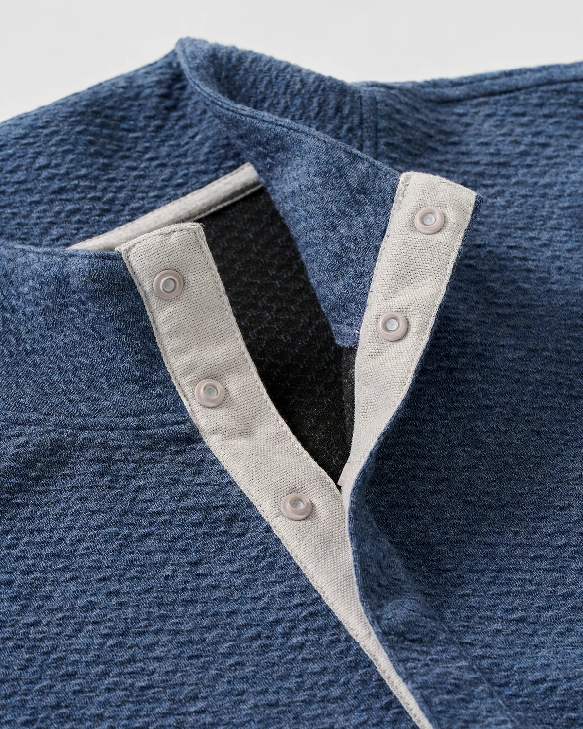 Close-up of the Johnnie-O Ransel Hidden Snap Pullover Big & Tall, a blue textured henley shirt by Johnnie-O, crafted with drirelease stretch fabric and featuring a light gray-trimmed placket with three visible hidden snap buttons.