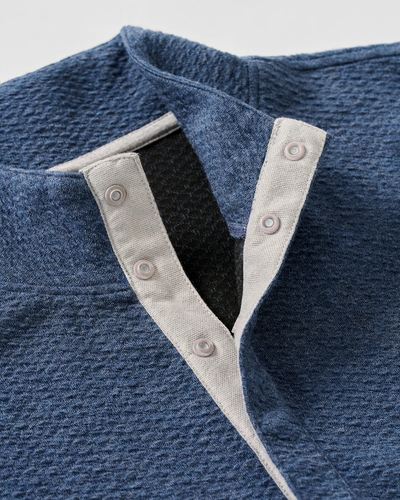 Close-up of the Johnnie-O Ransel Hidden Snap Pullover Big & Tall, a blue textured henley shirt by Johnnie-O, crafted with drirelease stretch fabric and featuring a light gray-trimmed placket with three visible hidden snap buttons.