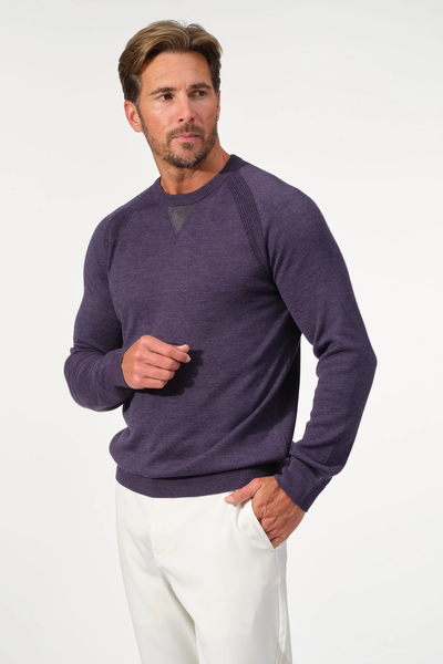 A man wears a Garnet Milano Crew Sweater 2522003CS, crafted from fine Italian yarn, and white pants. He stands against a plain light background with one hand in his pocket.