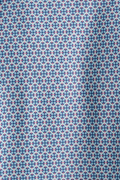 Blue and red geometric floral pattern on white fabric, shown in close-up with soft shadow—perfect to pair with tailored grey trousers or the Stone Rose APEX Medallion Geo shirt by Stone Rose.