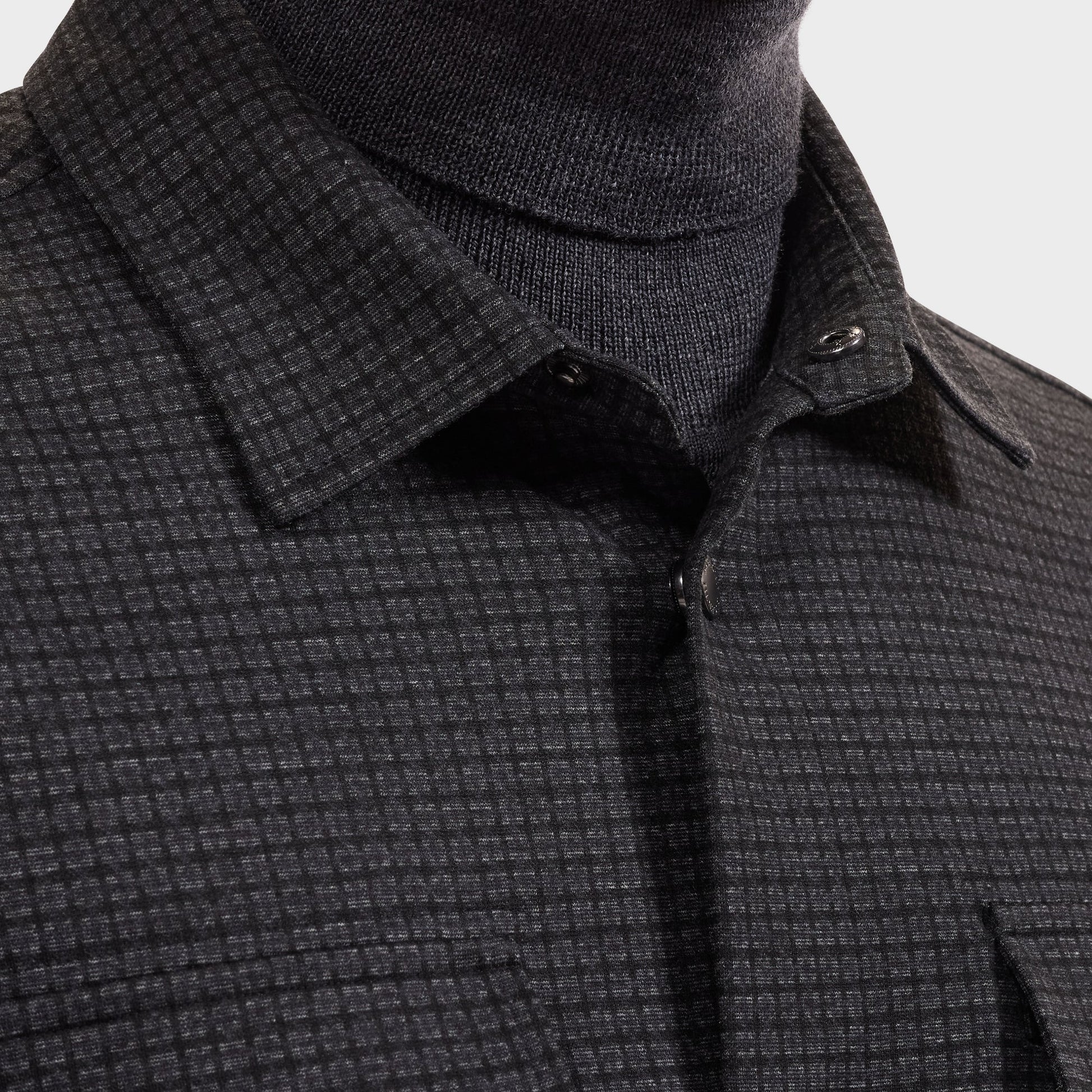 Close-up of a person wearing the Bugatchi Micro Check Knit Shirt KF2313K93 in dark gray over a black turtleneck, highlighting the shirt’s collar, buttons, and part of the chest area.