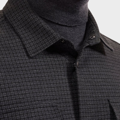Close-up of a person wearing the Bugatchi Micro Check Knit Shirt KF2313K93 in dark gray over a black turtleneck, highlighting the shirt’s collar, buttons, and part of the chest area.