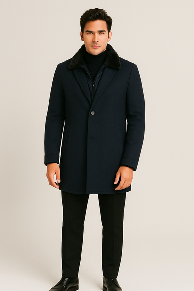 A man faces forward wearing the Paul Betenly Dino Travel Coat by Paul Betenly with a black fur collar, paired with black pants, a turtleneck, and shoes against a plain light background.