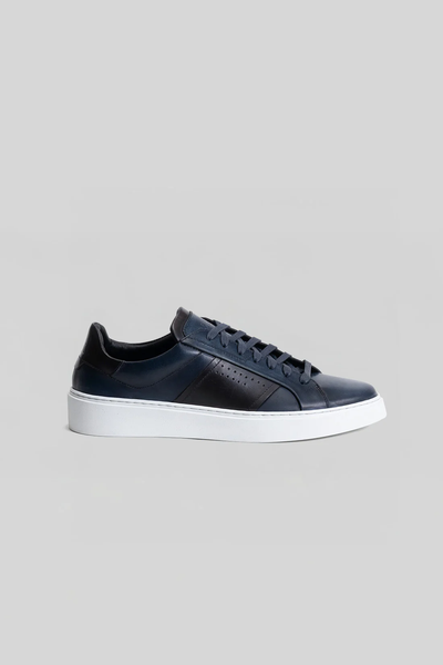 The Robert Barakett Dion Leather Sneaker by Robert Barakett features navy blue premium leather, black accents and laces, perforated side detail, and a white rubber sole, presented against a plain gray background.