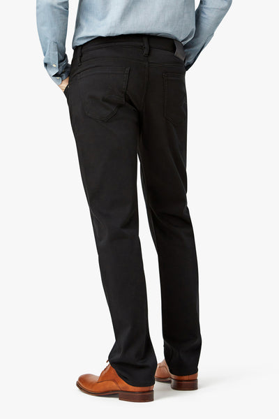 A person is shown from the back, standing against a plain white background, wearing 34 Heritage Courage Double Black pants, a light blue shirt, and brown shoes.