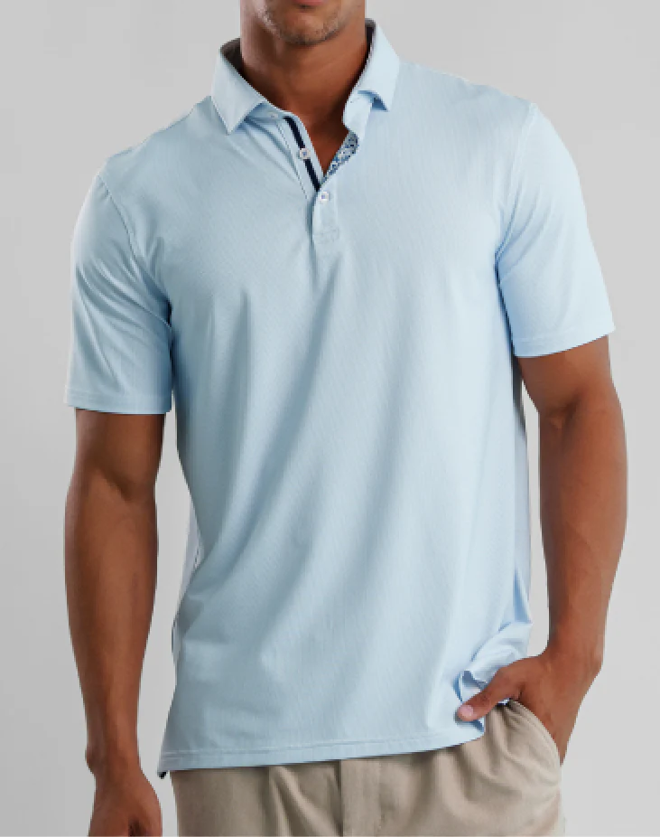 A man in a light blue Stone Rose Apex Birdseye Polo BSCSSP51 and beige pants stands with his left hand in his pocket—a modern classic addition to your summer wardrobe.