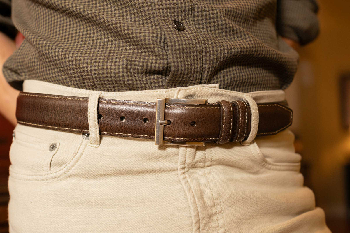 Someone wearing the Martin Dingman Bill Water Buffalo Leather Belt with light-colored pants and a dark plaid shirt.