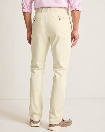 A man wearing Tommy Bahama Boracay Pant Big & Tall chinos in light beige and a light pink shirt with rolled sleeves, along with beige loafers, stands with his back to the camera.