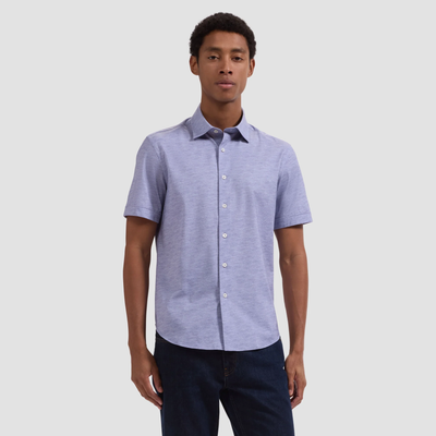 A man stands against a plain background wearing the Bugatchi Miles OoohCotton® Melange Shirt JF9505F40, featuring 8-way stretch, paired with dark jeans.