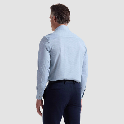 A man faces away from the camera, wearing a Bugatchi James Herringbone Sport Shirt HF9508K60 in light blue and dark dress pants, set against a plain background.