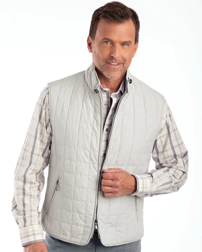 A man stands facing the camera, wearing the St. Croix Quilted Vest 7051 in light gray classic fit over a plaid shirt, adjusting the vest zipper with one hand.