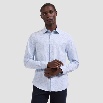 A man in a light blue patterned Bugatchi OP Jimmy OoohCotton® Shirt JF9648K61, made from wrinkle-resistant performance fabric, and dark pants stands before a plain light gray background.