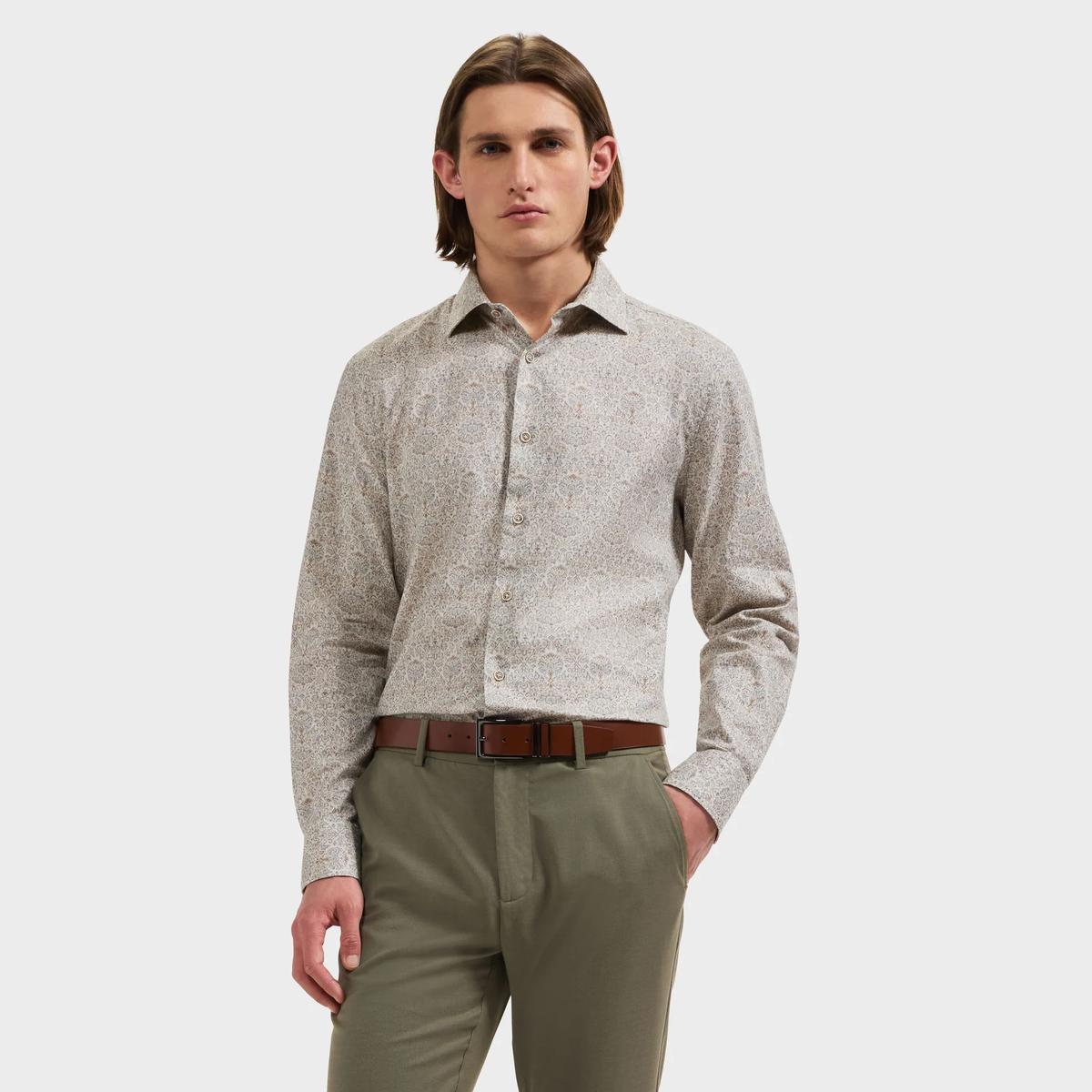 A person wearing the Bugatchi Axel Paisley Sport Shirt by Bugatchi, styled with olive green pants and a brown belt, stands against a plain white background.