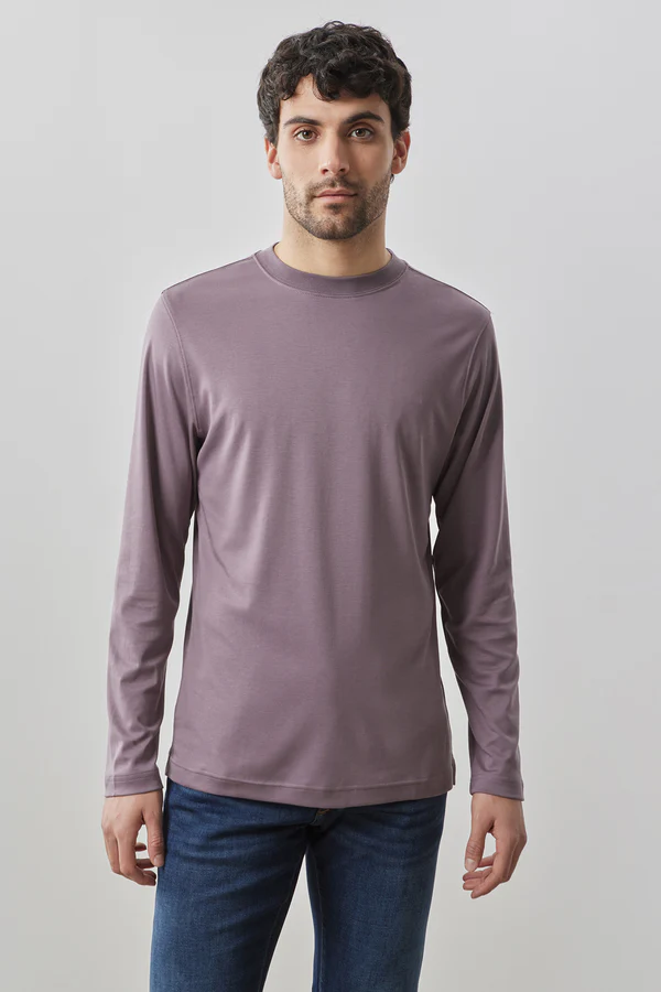 A man stands against a plain background, wearing a Robert Barakett High Crew Long Sleeve RB82247 shirt in mauve and blue jeans.