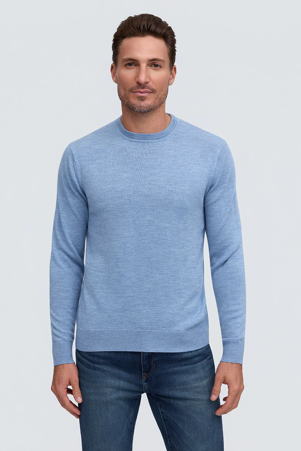 A man wearing a light blue Raffi Merino Classic Crew Neck HWC19392 sweater and dark wash jeans.