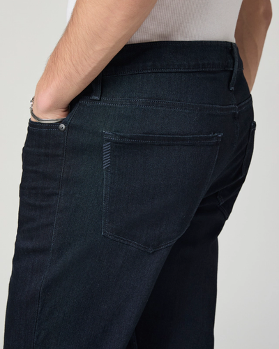 A person wearing Paige Federal Straight Slim Jeans in a modern slim fit and a white ribbed tank top, with one hand in their back pocket.
