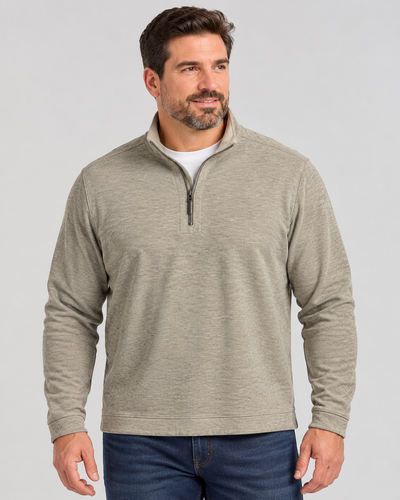 A man wears a beige Tommy Bahama Flipview 1/2 Zip Reversible Sweatshirt Big & Tall over a white t-shirt and blue jeans.