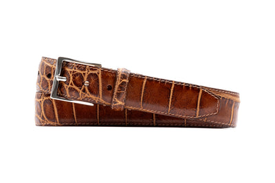 Martin Dingman Perry Alligator Grain Belt by Martin Dingman, featuring a brown alligator pattern and silver buckle, rolled up on a white background.