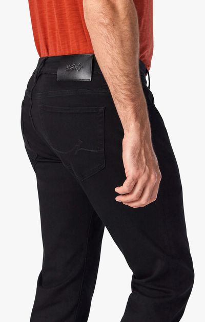 A man in a red shirt wears 34 Heritage Courage Black Urban Jeans, showing the back and right arm, with pocket, waistband label, and straight leg fit from 34 Heritage on display.