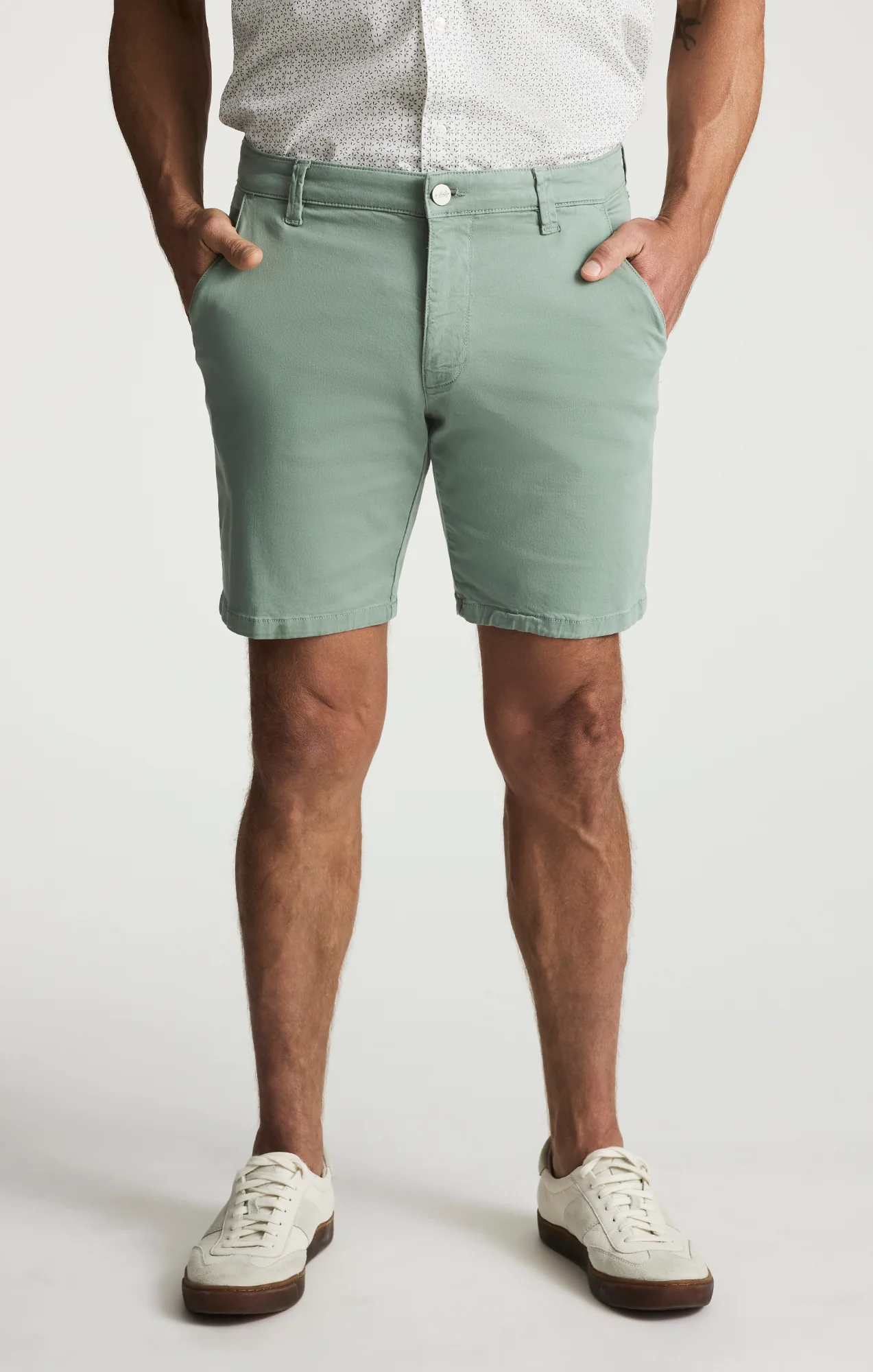 Man wearing 34 Heritage Arizona Twill Short in mint green, a white short-sleeve button-up shirt, and white sneakers, standing with hands in pockets against a plain background.