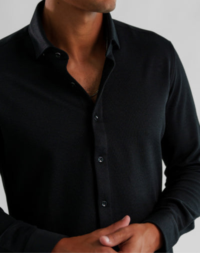 A man wearing a black Stone Rose ORIGIN - Long Sleeve Tech Pique Shirt with a collar.