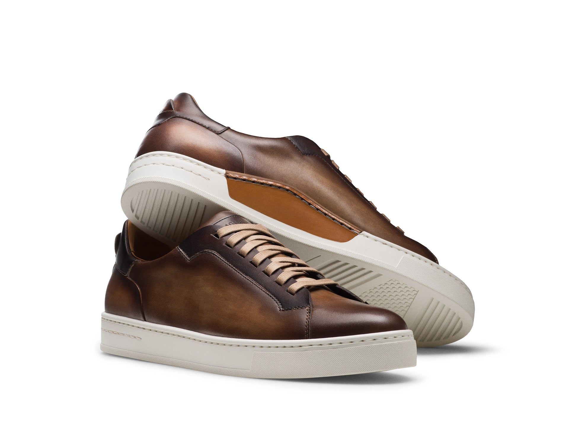 The Magnanni Amadeo Sneaker by Magnanni features brown sporty leather with white soles; one shoe stands upright while the other lies on its side, showcasing both the sole and side profile.