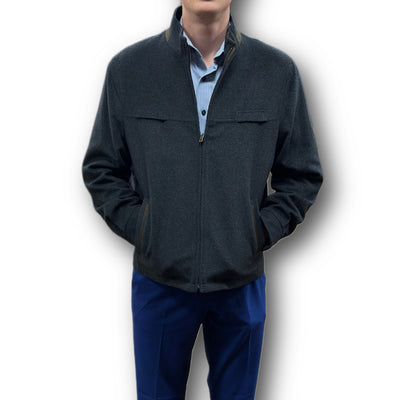 A man stands with hands in his Enzo Coat Play pockets—an elegant dark zip-up jacket from Enzo—worn over a light blue collared shirt and blue pants, set against a white background.