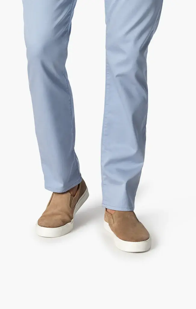 A person models the 34 Heritage Courage Coolmax modern straight leg light blue pants by 34 Heritage with tan slip-on shoes featuring white soles, standing against a plain white background.