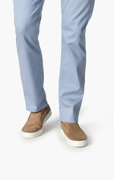 A person models the 34 Heritage Courage Coolmax modern straight leg light blue pants by 34 Heritage with tan slip-on shoes featuring white soles, standing against a plain white background.