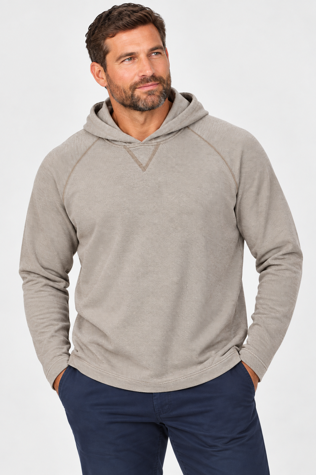 A man with short brown hair and a beard is wearing the Johnnie-O Cotton Knit Hoodie Big & Tall—a beige quarter-zip pullover sweatshirt from Johnnie-O crafted with moisture-wicking drirelease fabric—paired with navy pants, standing with his hands in his pockets against a plain light background.