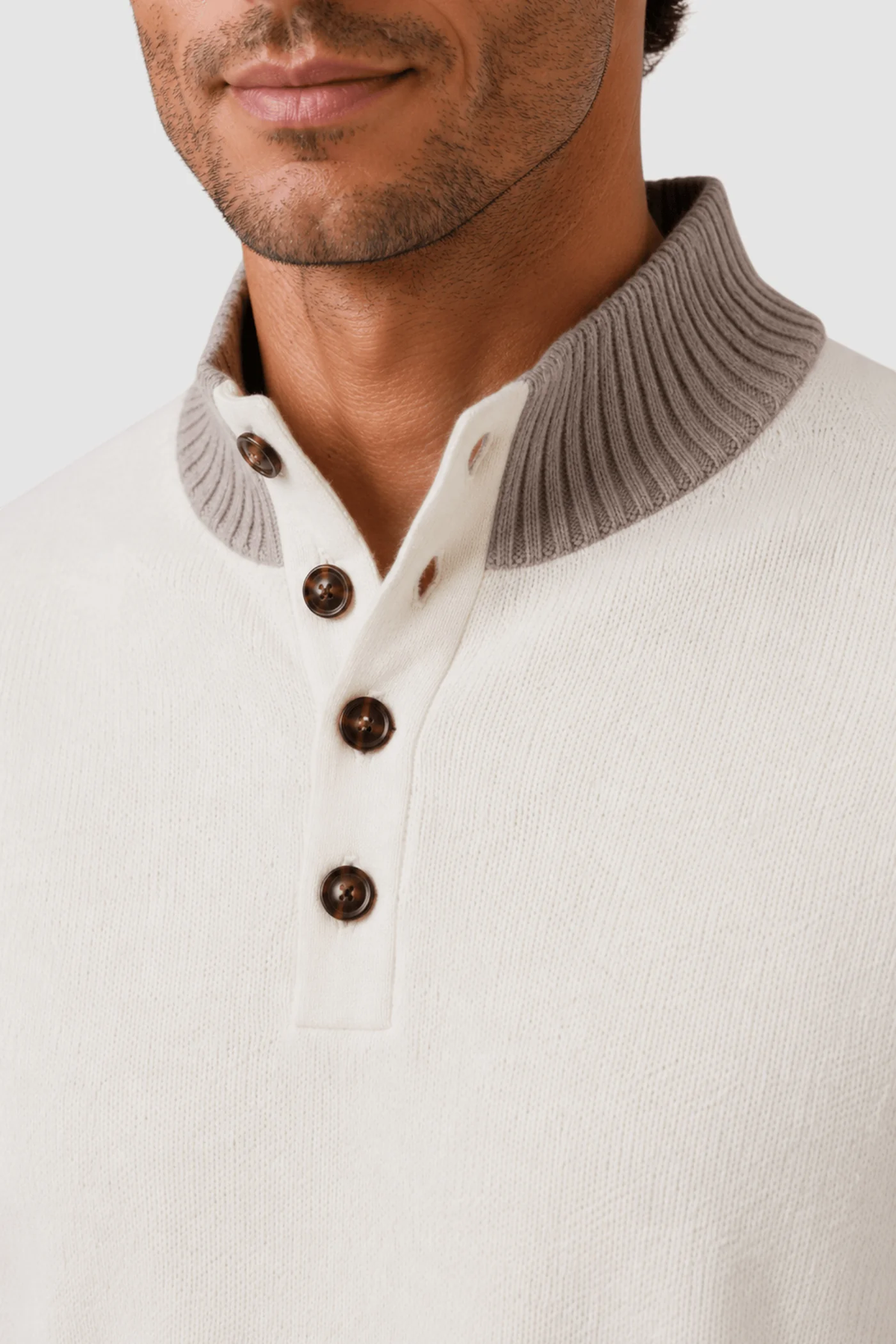 A man wears the Garnet Tate Contrast-Trim Mock Neck Sweater 2622022 by Garnet, a refined men’s wool-blend sweater in cream with a ribbed gray mock neck collar and four brown buttons on the placket, exemplifying sophisticated style.