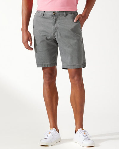 A person wearing a pink shirt, white sneakers, and Tommy Bahama Boracay Shorts Big & Tall by Tommy Bahama stands against a plain white background.